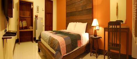 A bedroom with a wooden bed, a bedside table with a lamp, a chair, a wardrobe, and a television.