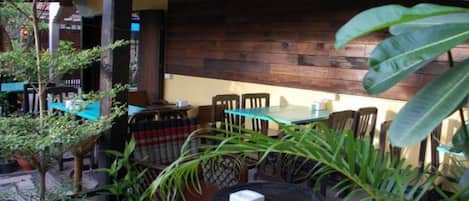 An outdoor seating area with wooden tables and chairs, surrounded by potted plants and a wooden wall.