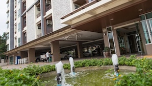 A multi-story building with a covered parking area and a water feature in the foreground. - Central place serviced apartment 1 (Chonburi)