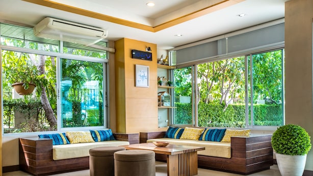 A modern living room with a large window, built-in seating, a coffee table, and a potted plant. - Central place serviced apartment 1 (Chonburi)