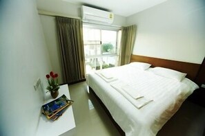 Een hotelkamer met een bed, een nachtkastje met een boek en een bloemetjesvaas, en een raam met gordijnen.