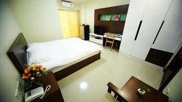 A hotel room with a bed, a desk, a chair, a small table, and a wardrobe.