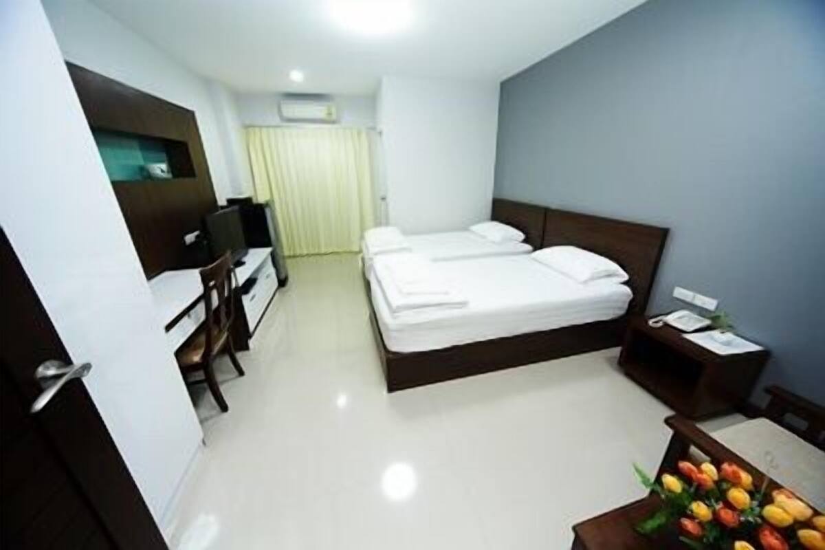 Habitación de hotel con cama, escritorio, silla, una mesita con un florero y una ventana con cortinas.