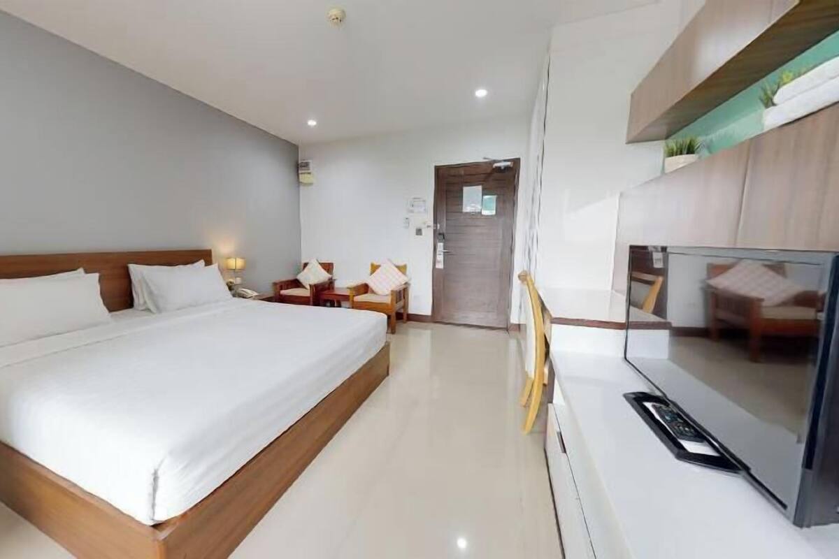 Habitación de hotel con cama, mesitas de noche, televisión y un pequeño escritorio con silla.