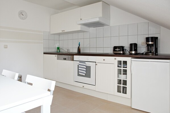 A compact kitchen with white cabinets, a built-in oven, a coffee maker, and a clock on the wall. - City Park Apartments Ludi (Leipzig)