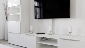 Un salon moderne avec un téléviseur à écran plat fixé au mur, un meuble blanc avec des tiroirs et deux chandeliers posés sur la commode.