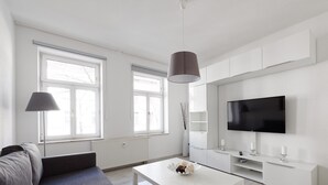 Un salon moderne avec un canapé gris, une table basse blanche et un téléviseur à écran plat fixé au mur.