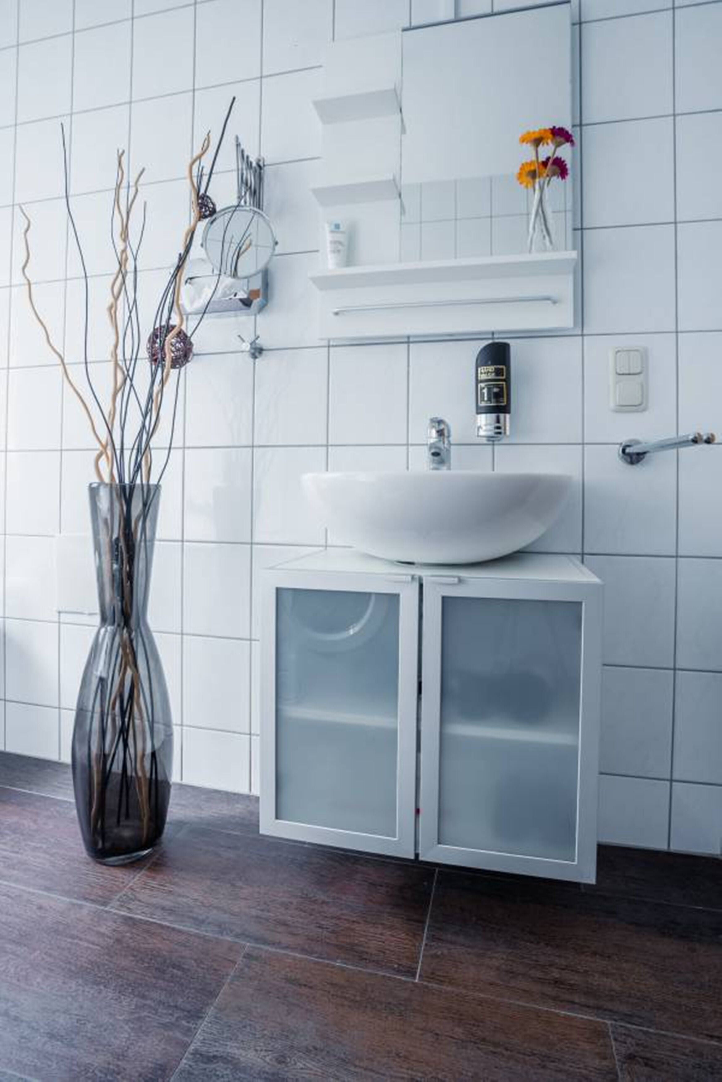 A modern bathroom with a white sink, a mirror, and a cabinet with frosted glass doors.