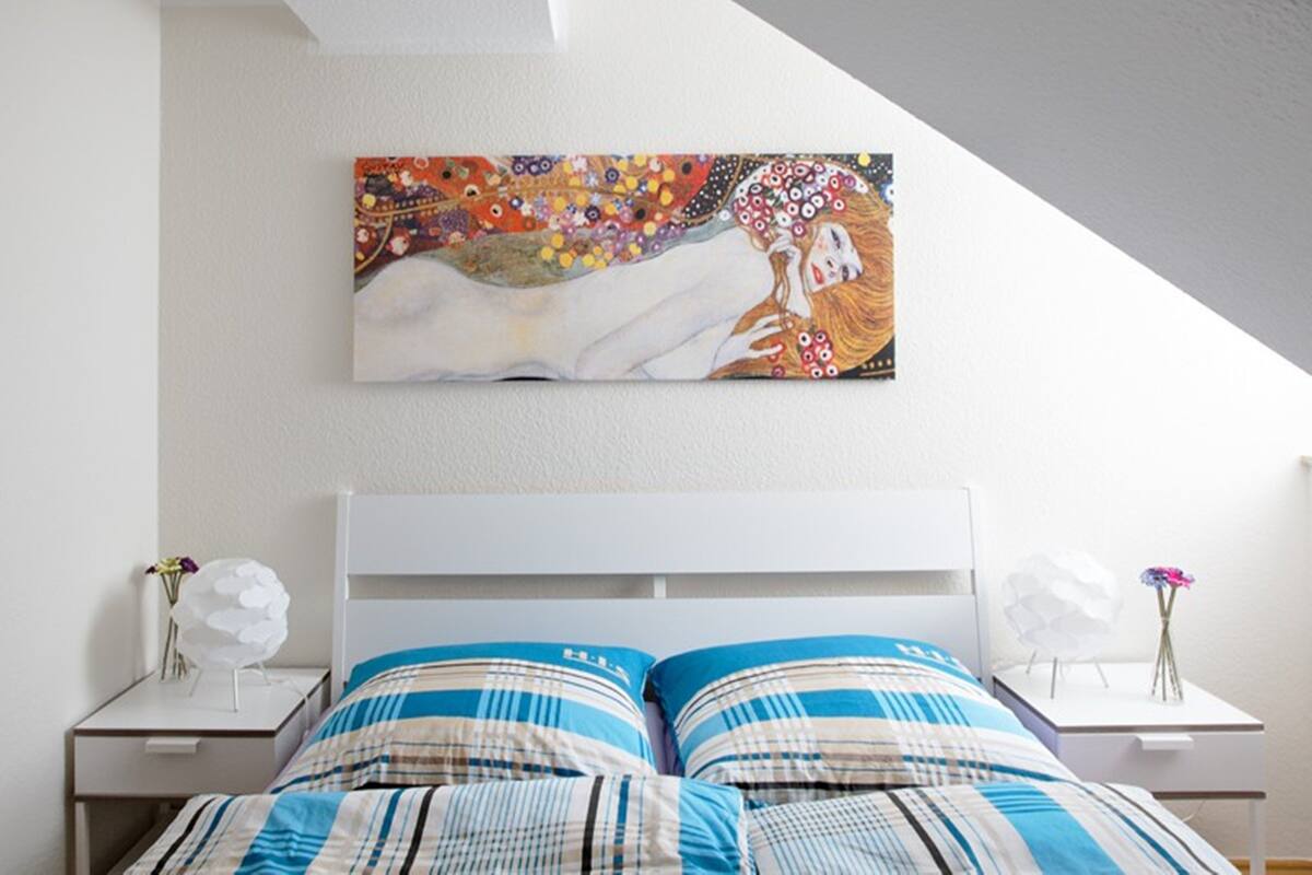 Une chambre à coucher avec une tête de lit blanche, un lit recouvert d’une literie à rayures et un tableau coloré accroché au-dessus du lit.