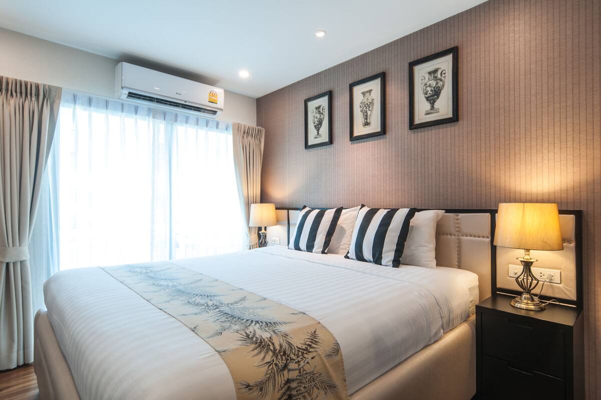 Ein Hotelzimmer mit einem großen Bett, zwei Nachttischen, einer Wand-Klimaanlage und gerahmten Kunstwerken.