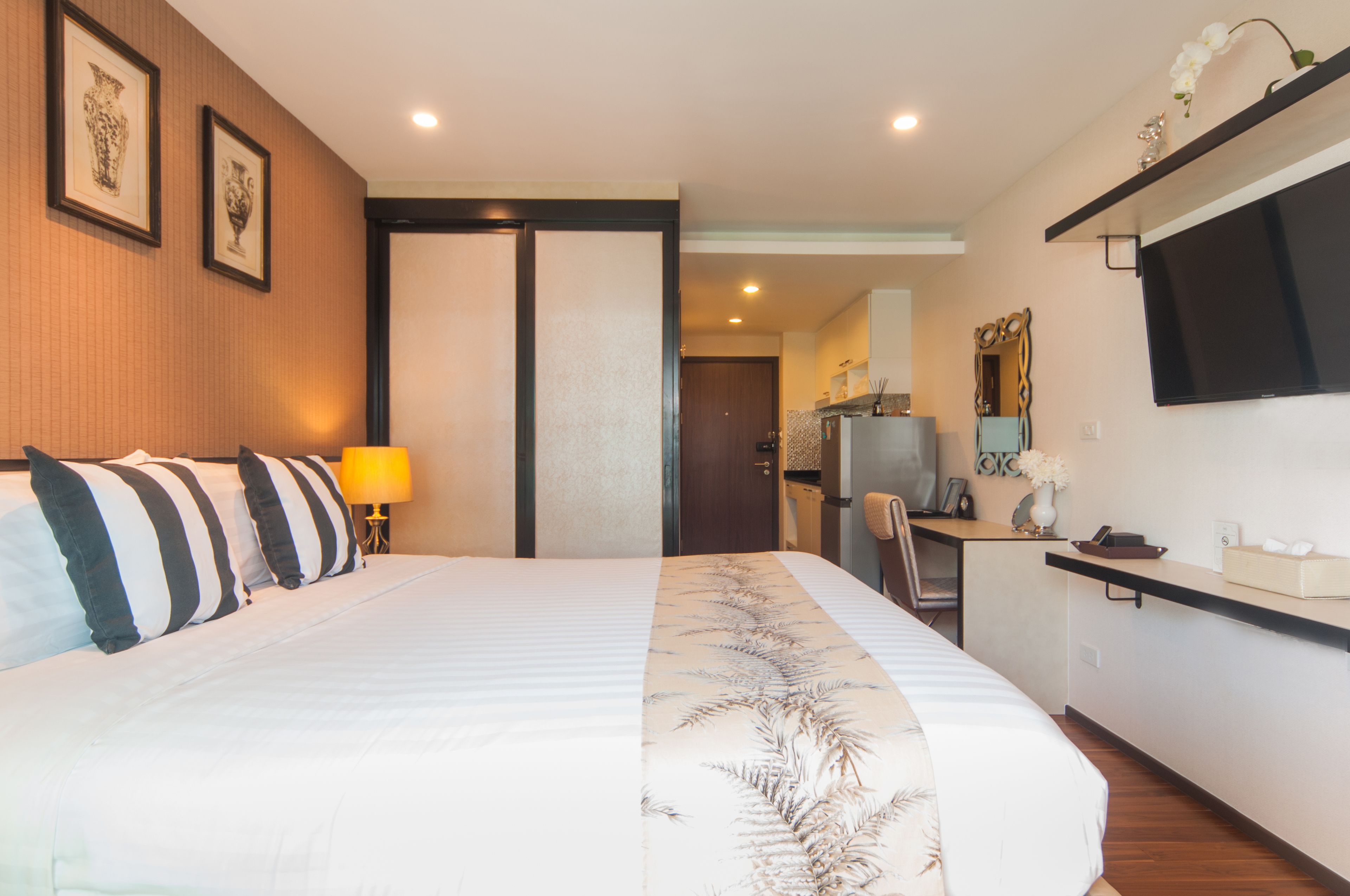 A hotel room with a bed, a desk, a chair, a TV, and a door leading to a bathroom.