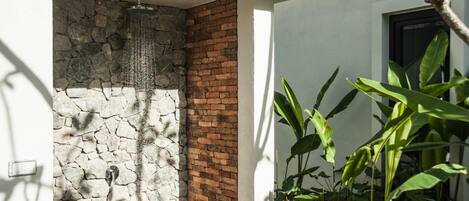 A modern outdoor shower area with a stone wall and brick section, surrounded by lush greenery.