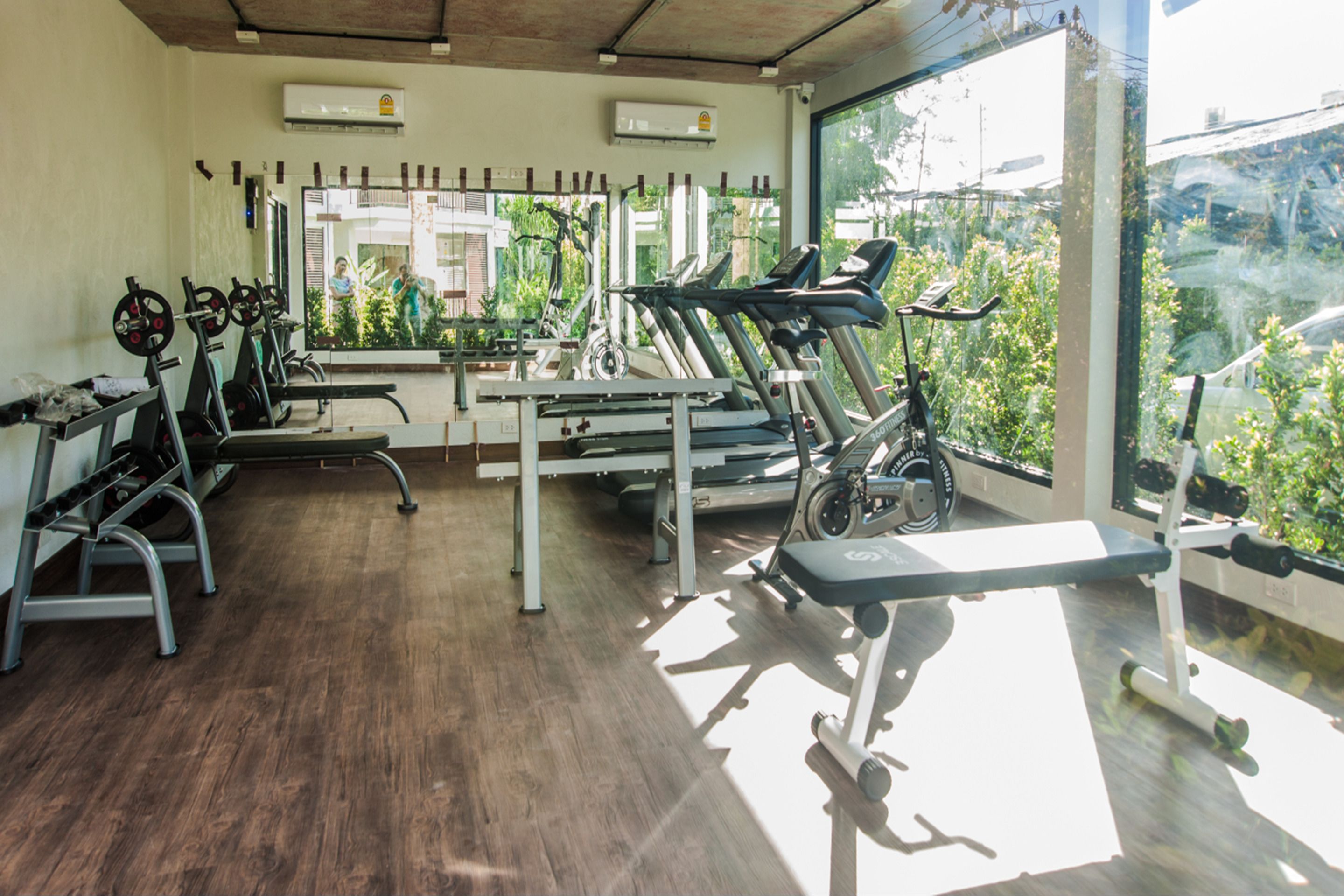 A gym with various exercise equipment, large windows, and a view of greenery outside.