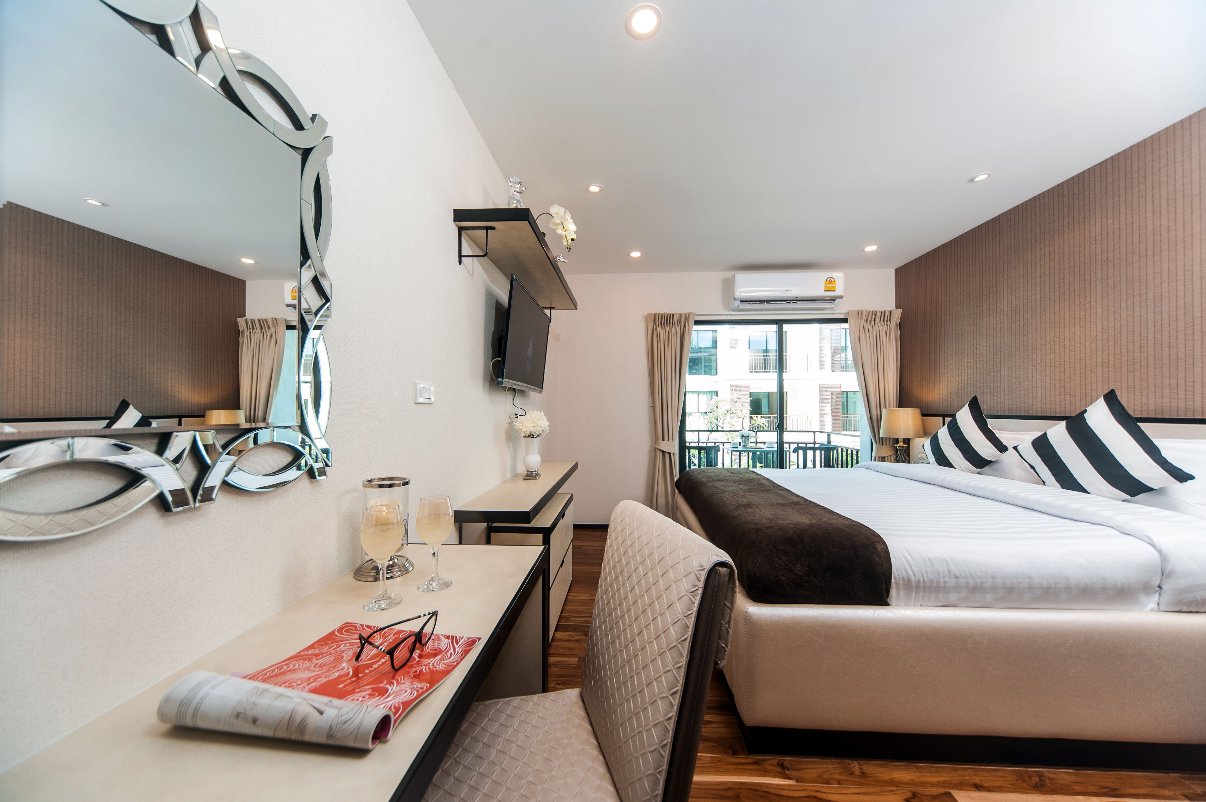 A modern hotel room with a large bed, a desk with a chair, a TV, and a window with curtains.