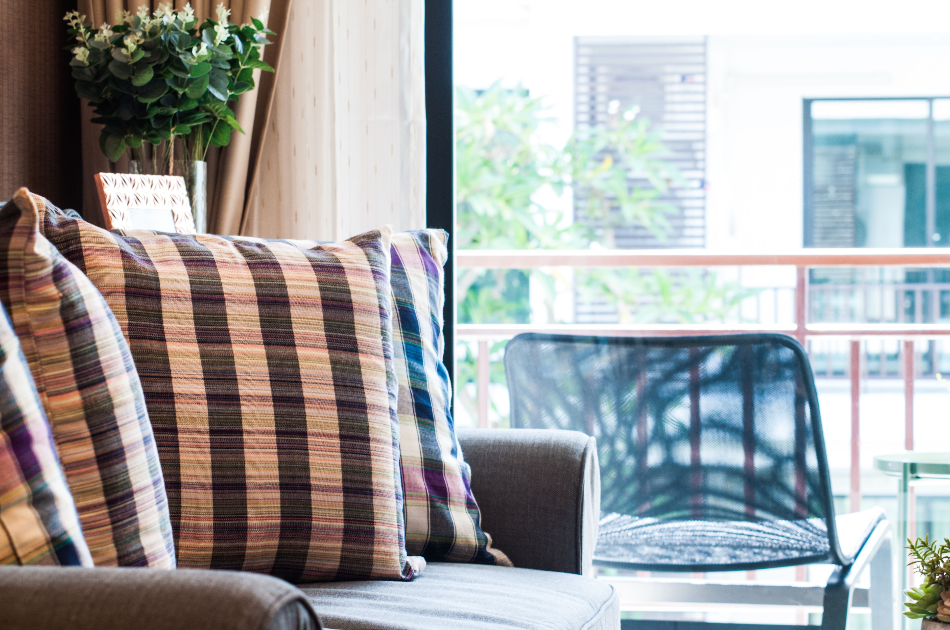 A sofa with plaid cushions, a chair, and a view of buildings and greenery through a window.