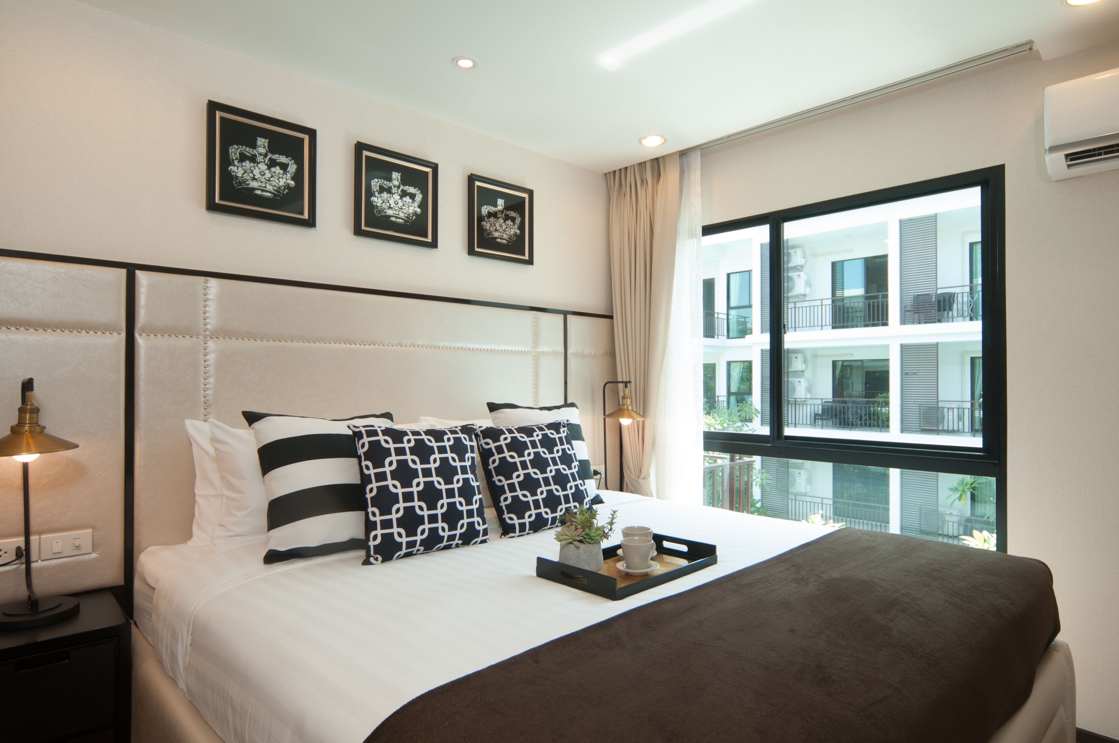 A modern hotel room with a large bed, a nightstand with a lamp, and a window with a view of the building's exterior.