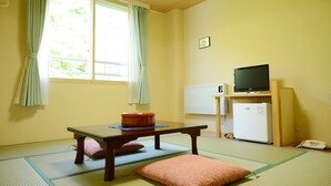 Una habitación con esteras de tatami, una mesa baja con cojines, un televisor, un refrigerador y un teléfono.