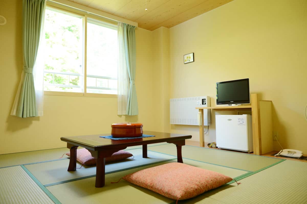 A room with tatami mats, a low table with cushions, a television, a refrigerator, and a phone.