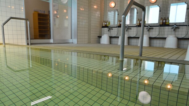 Una piscina con pisos y paredes de azulejos, una barandilla de metal y una barrera de cristal.