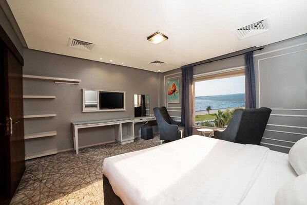 A hotel room with a bed, a desk, a chair, a TV, and a view of the ocean.