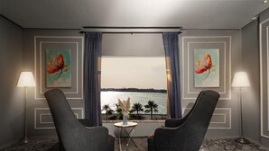 Ett rum med två fåtöljer placerade framför ett fönster med utsikt över en vattenyta, ett litet runt bord med en vas och två lampor.