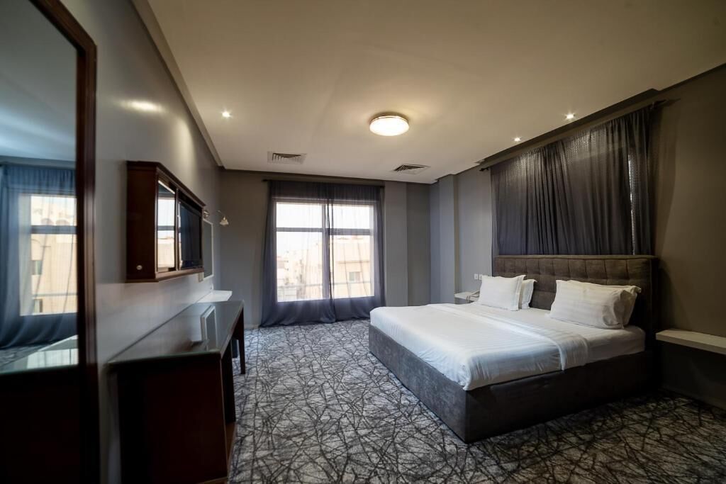 Une chambre d’hôtel avec un grand lit, un bureau, un miroir et une fenêtre avec des rideaux.