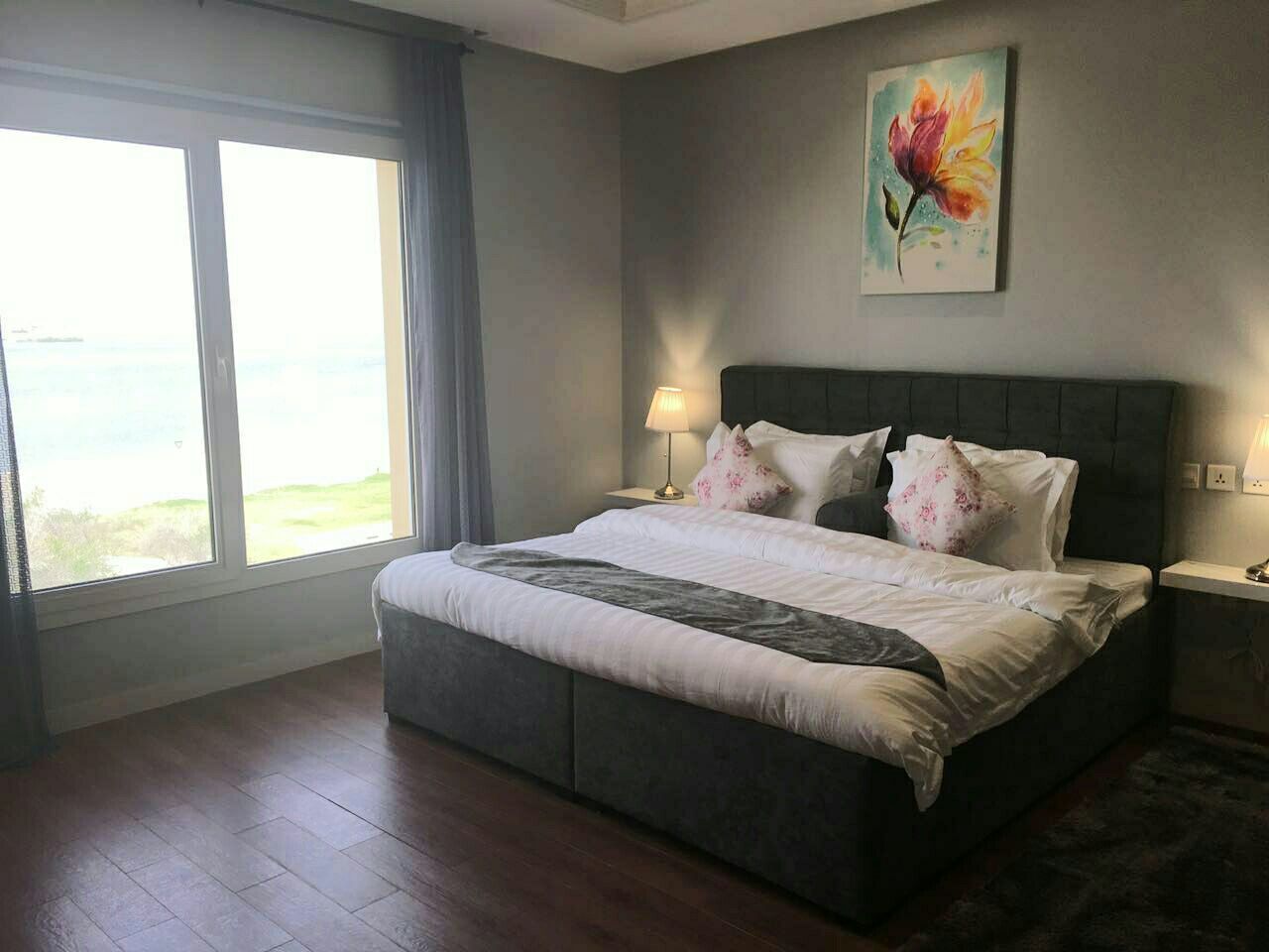 Un dormitorio con una cama grande, una mesita de noche, una lámpara y un cuadro en la pared.