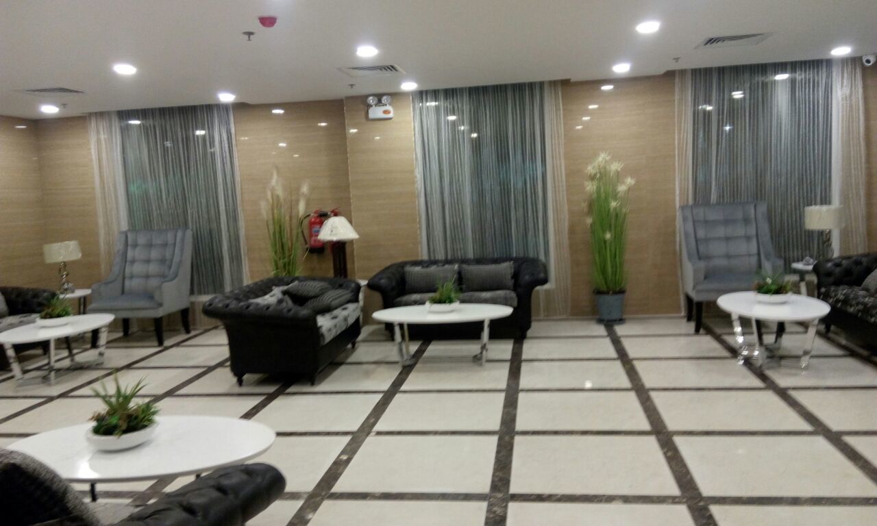 A modern lobby with a checkered floor, two sofas, two armchairs, and two small tables with potted plants.