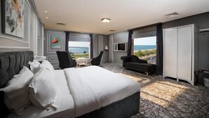 Ett hotellrum med en stor säng, en soffa, en TV och utsikt över havet.