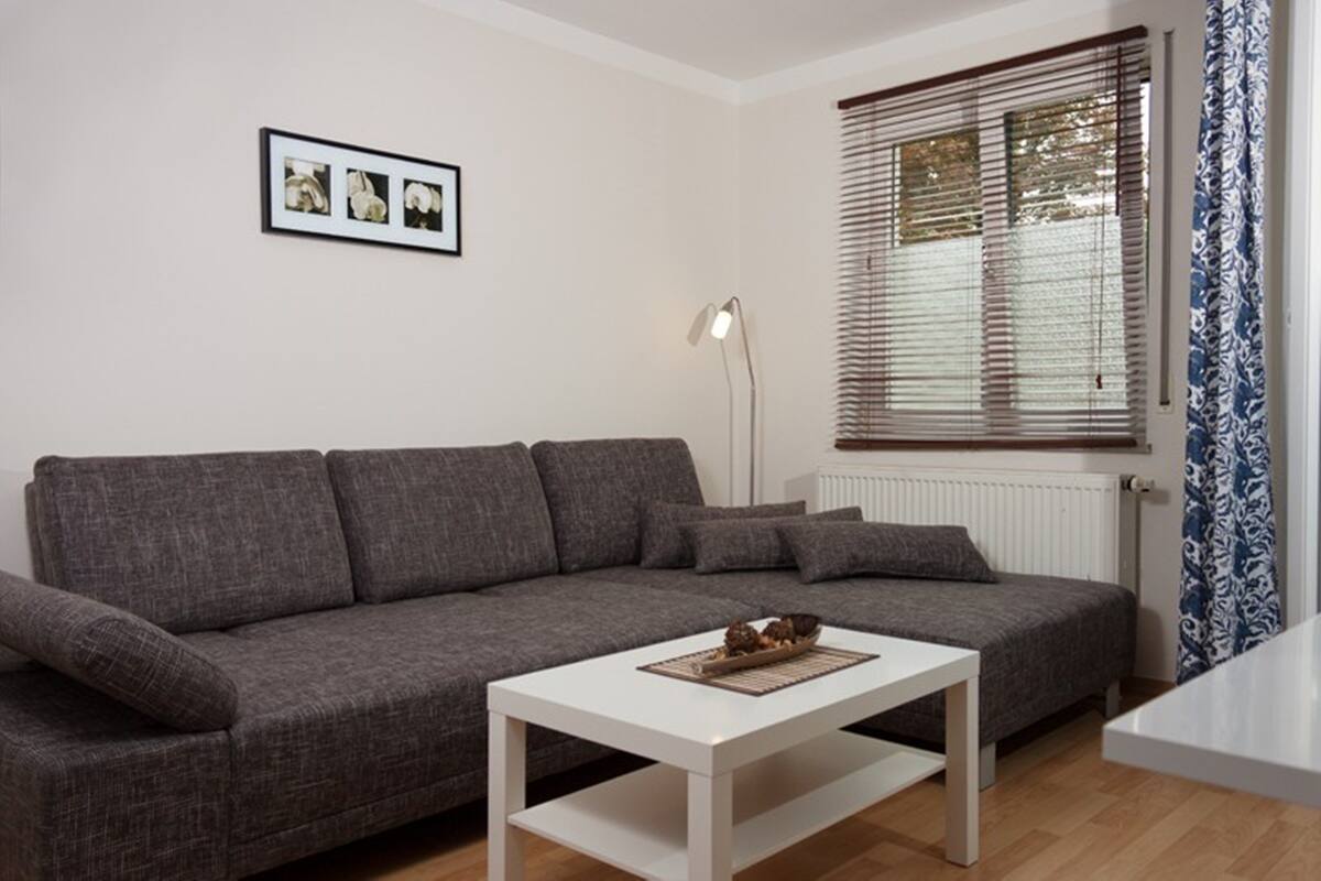 A living room with a grey sofa, a white coffee table, a floor lamp, and a window with blinds.