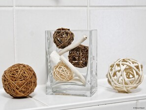 A clear glass container with three spherical objects made of twine and white material, placed on a white surface against a white tiled background. - City Park Apartments Reichi (Leipzig)
