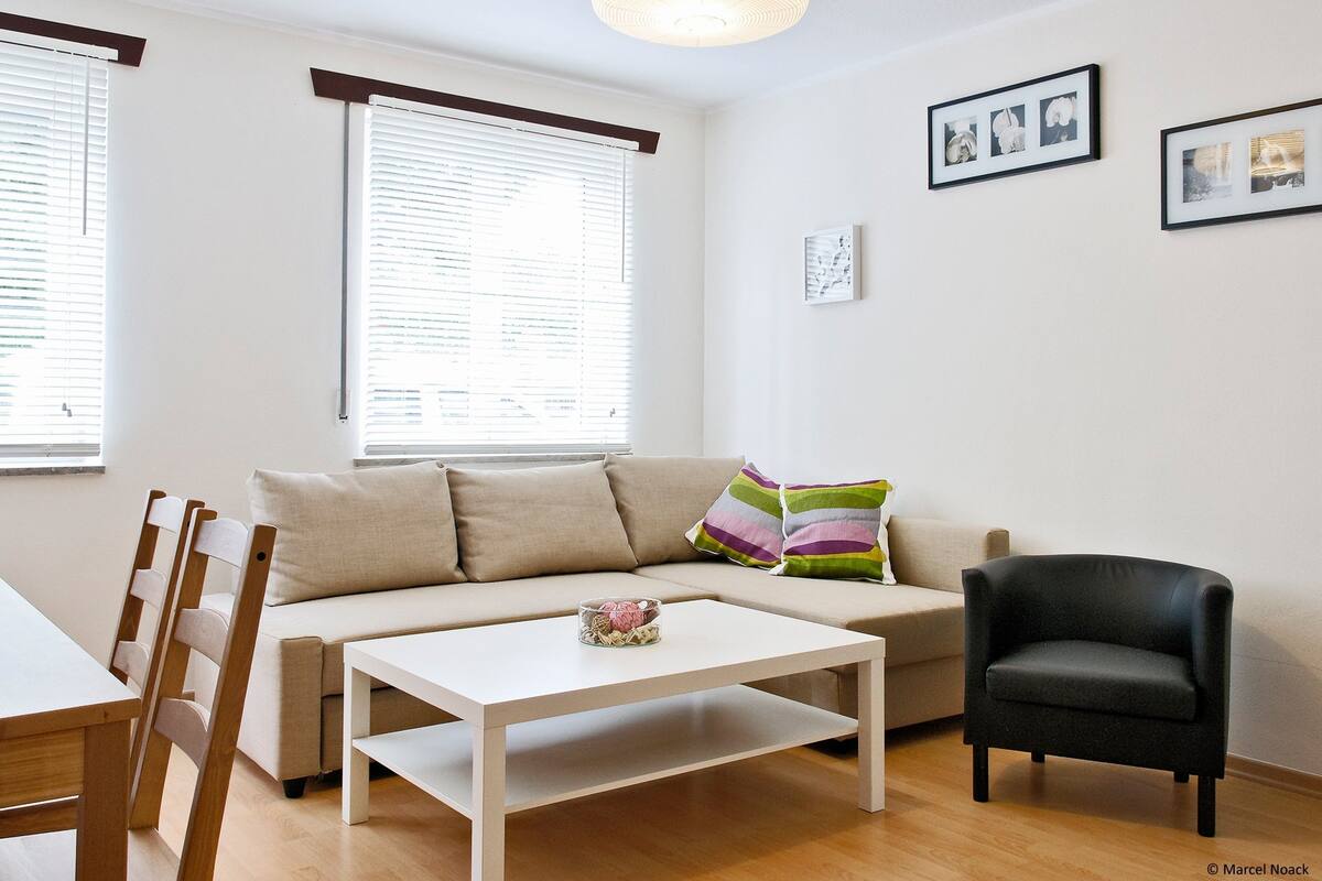 A living room with a sofa, a black armchair, a white coffee table, and a lamp.