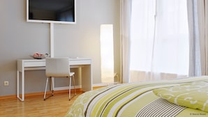 Un dormitorio con cama, escritorio, silla, televisor y ventana con cortinas.