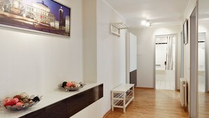 Un pasillo moderno de hotel con suelo de madera, una recepción con un cuenco decorativo, un cuadro de un paisaje urbano enmarcado y un espejo que refleja la habitación.