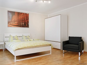 A modern bedroom with a bed, a chair, a wardrobe, and a painting on the wall.
