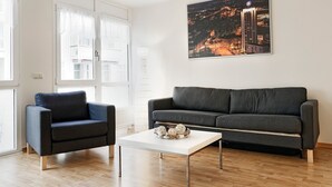 Una sala de estar moderna con un sofá gris, una mesa de centro blanca y una pintura de un paisaje urbano en la pared.