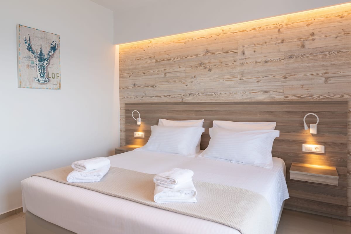 Een moderne hotelkamer met een houten hoofdbord, wit beddengoed en twee bedlampjes.