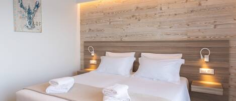 A modern hotel room with a wooden headboard, white bedding, and two bedside lamps.