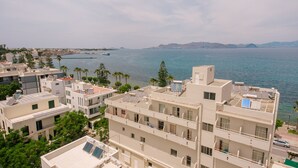A coastal residential area with modern buildings, some with solar panels, and a view of the sea and distant mountains. - Orpheus Studios (Kos)