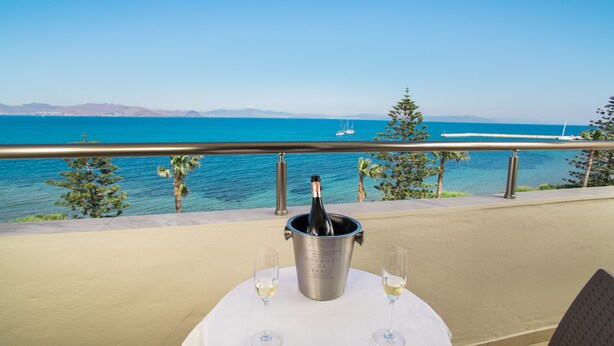 A table with a bottle of champagne and two glasses on a balcony overlooking a body of water with boats. - Orpheus Studios (Kos)