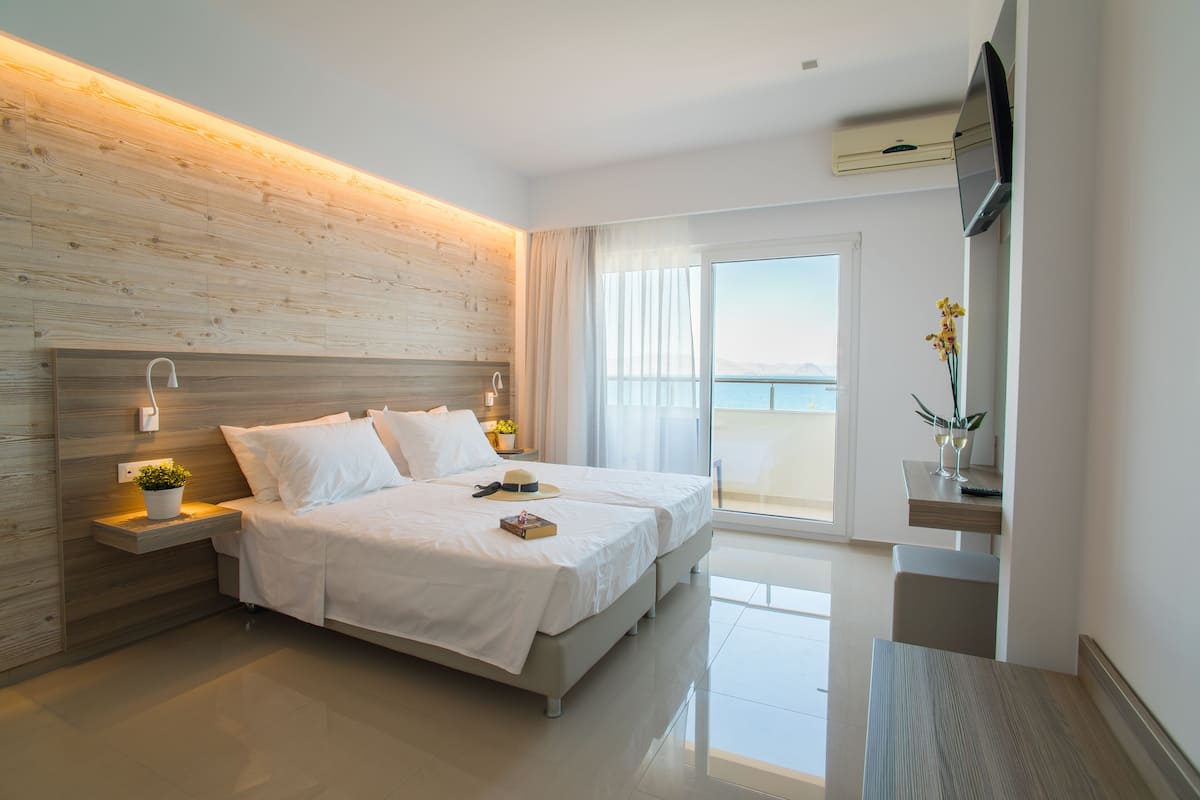 Een moderne hotelkamer met een groot bed, nachtkastjes met lampen, een flatscreen televisie en uitzicht op zee.