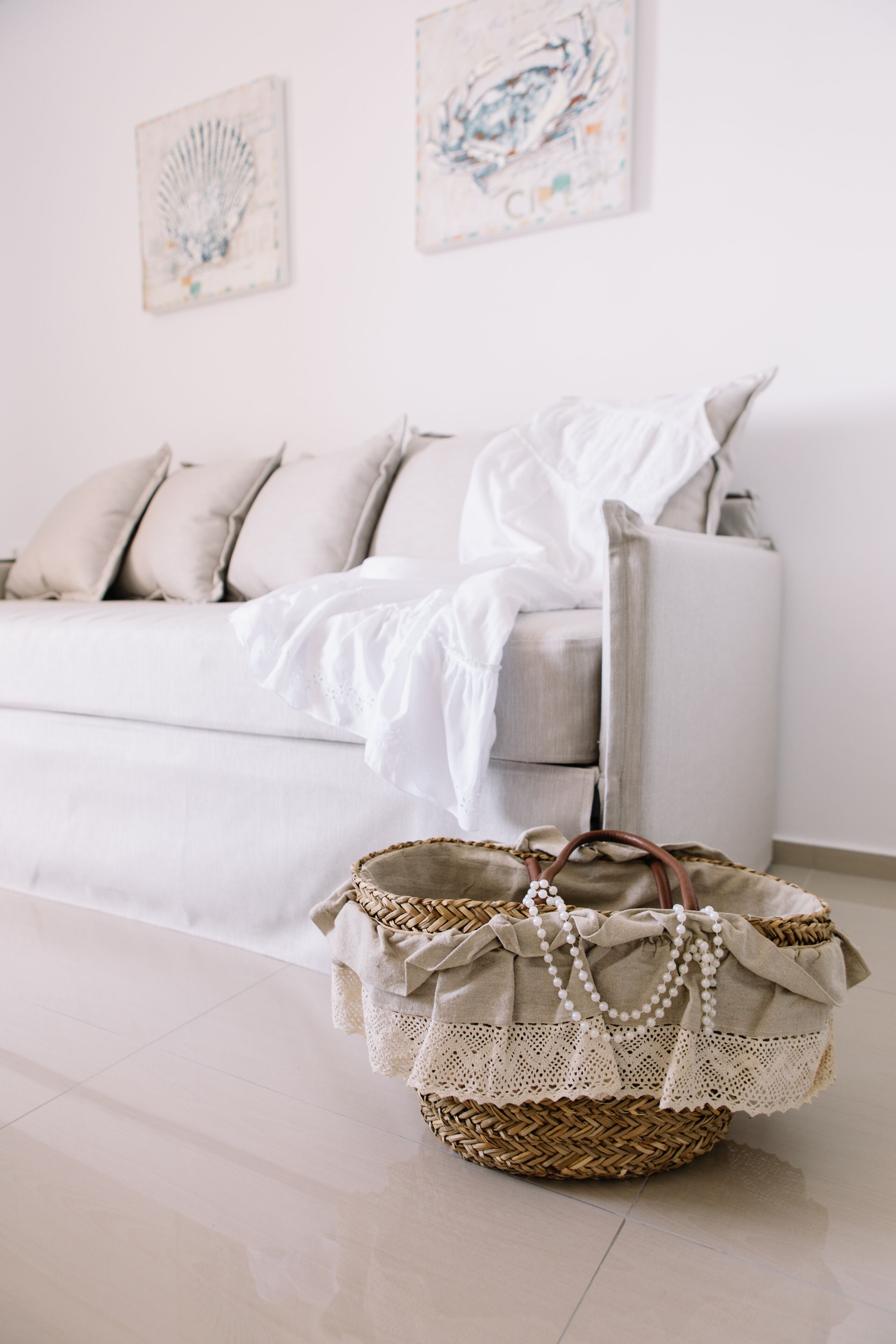 A room with a white sofa, a woven basket with a white cloth and beads, and two abstract paintings on the wall.