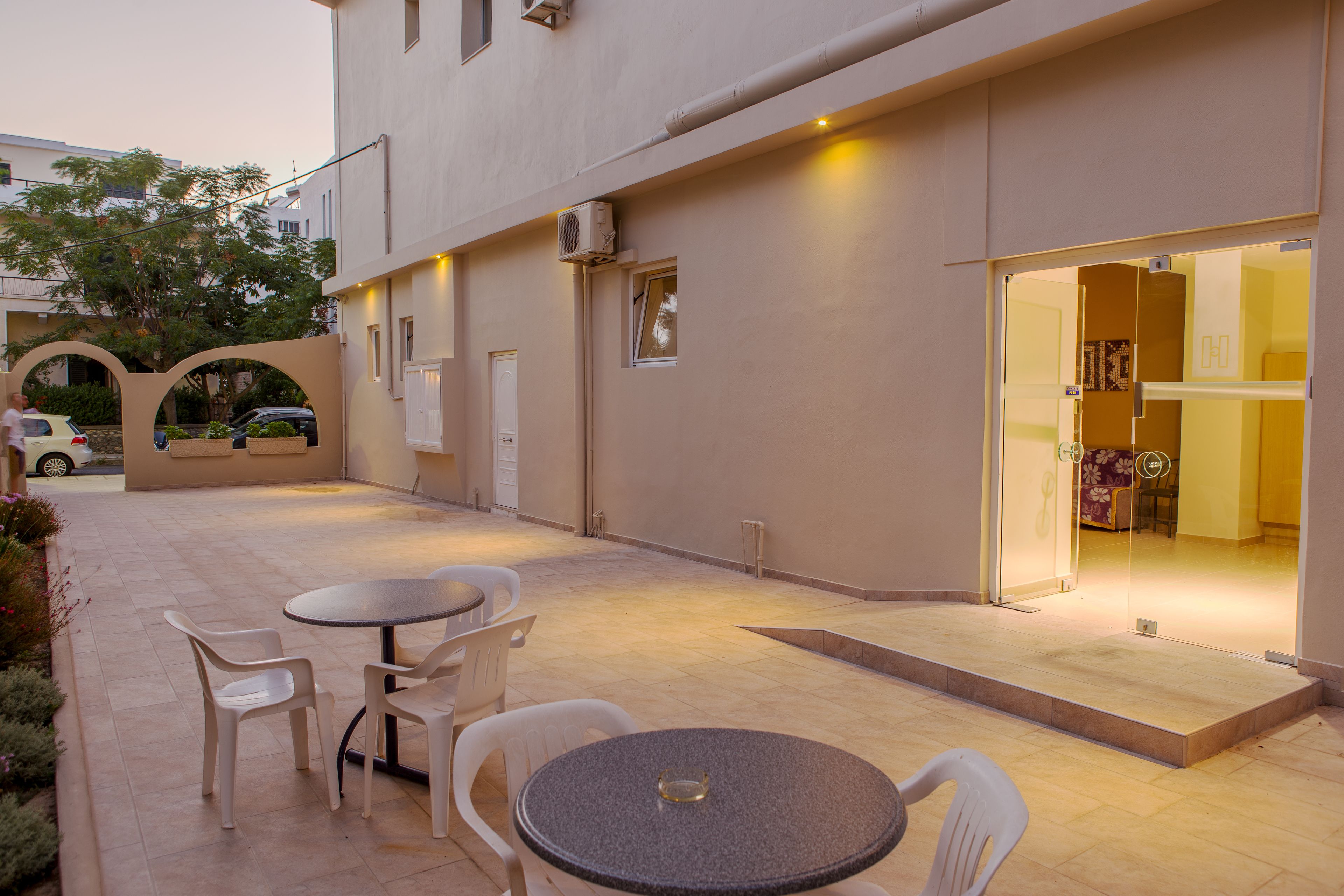 An outdoor patio with a round table and chairs, a covered walkway, and a building entrance with glass doors.
