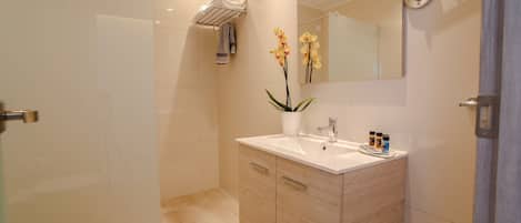 A modern bathroom with a glass shower enclosure, a white sink with a vase of flowers, and a large mirror above the sink.