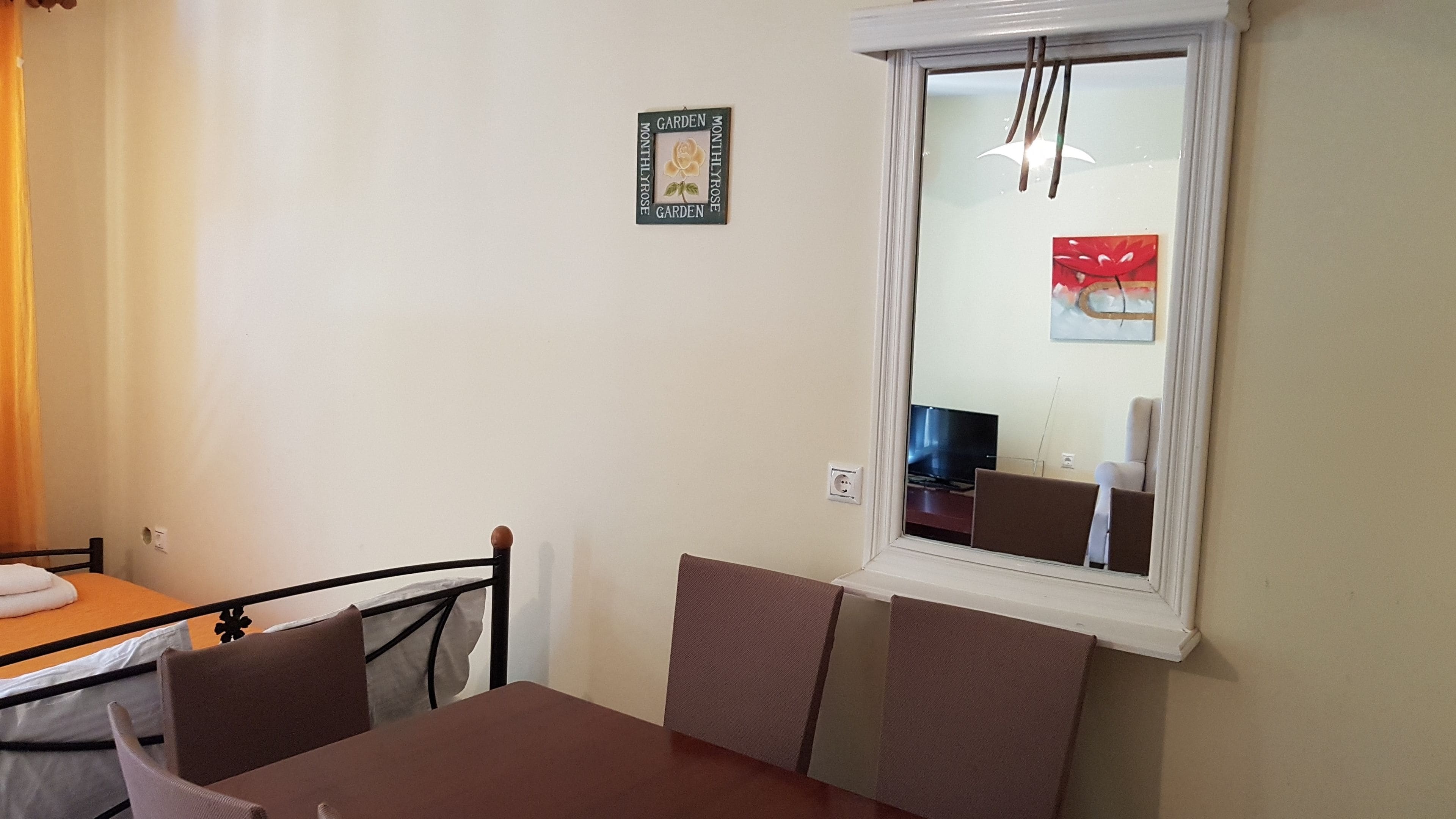 Un petit coin repas avec une table et des chaises, une fenêtre donnant sur l’intérieur et un cadre photo fixé au mur.