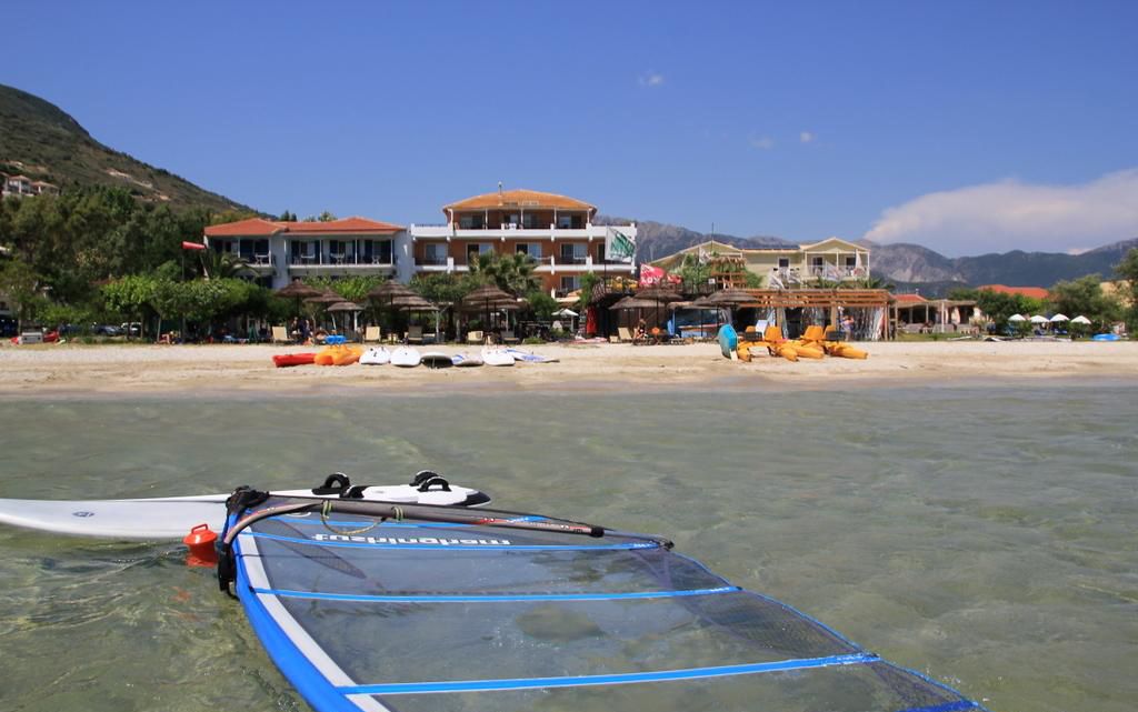 Vista de la playa con agua cristalina, una tabla de surf y edificios al fondo.