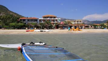 Vista de la playa con agua cristalina, una tabla de surf y edificios al fondo.