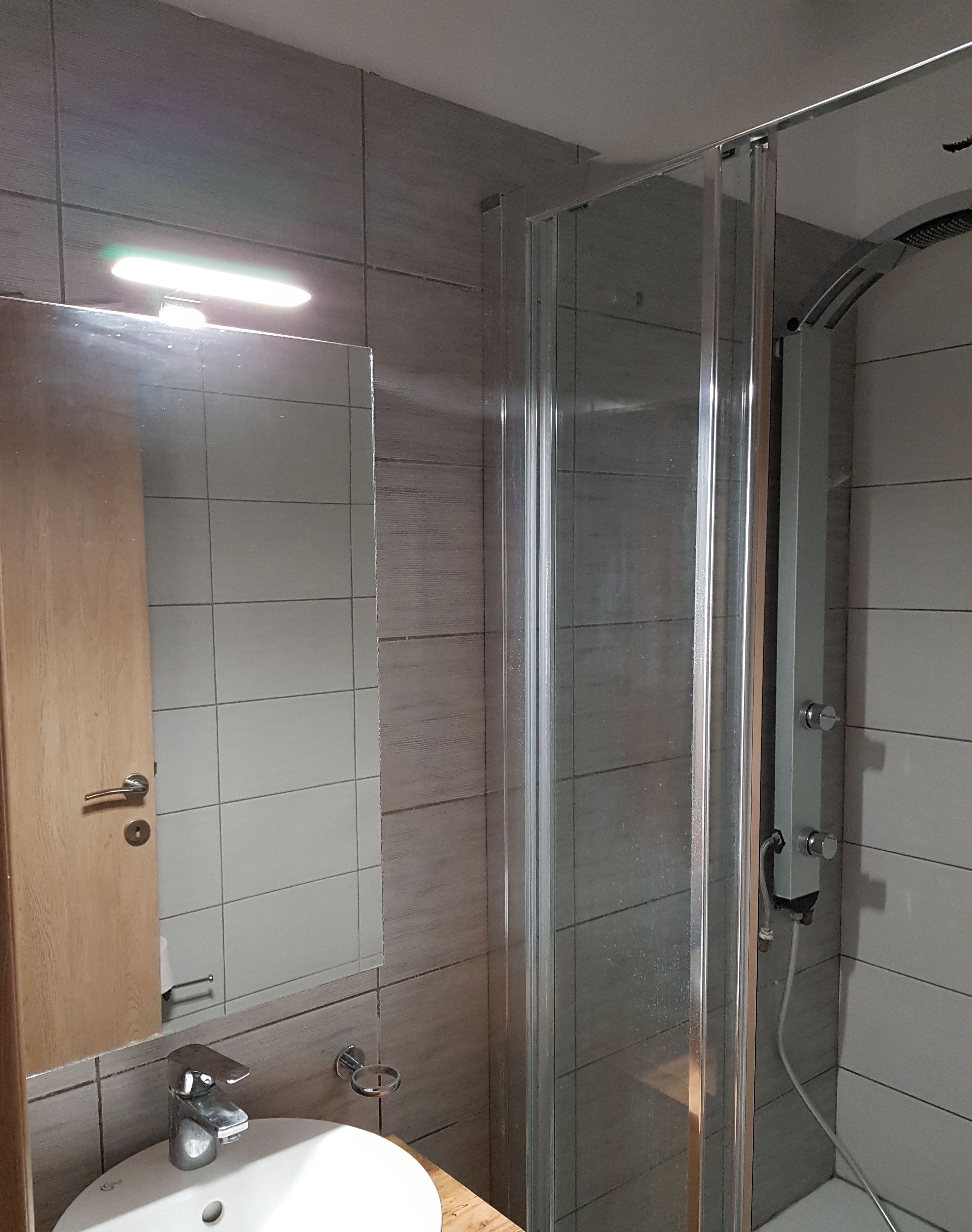 A modern bathroom with a glass shower enclosure, a sink with a mirror, and tiled walls.