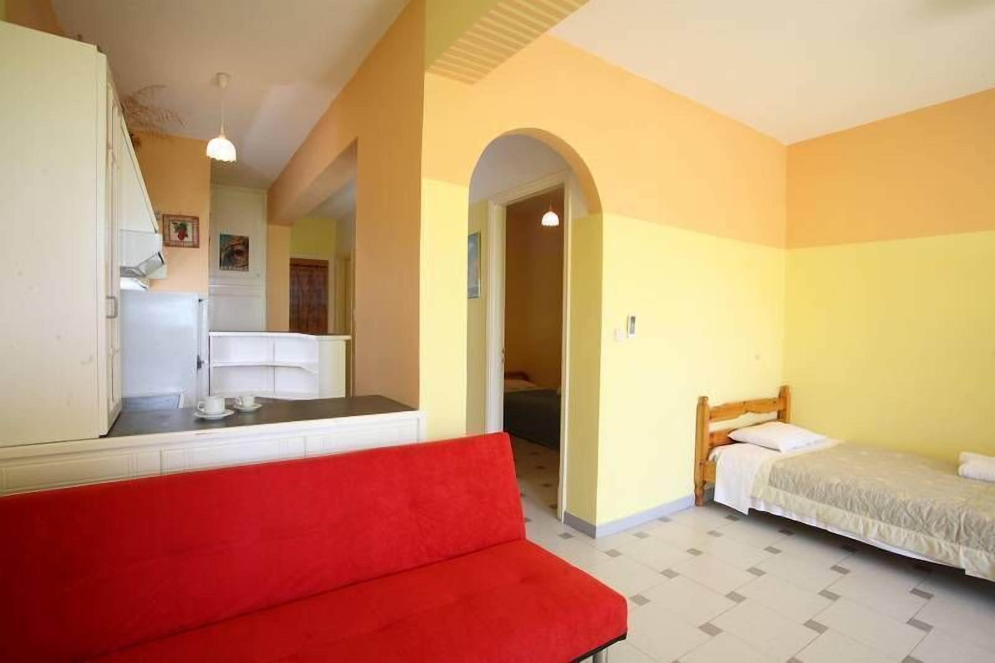 A room with a red sofa, a bed, a white wardrobe, and a small kitchenette.
