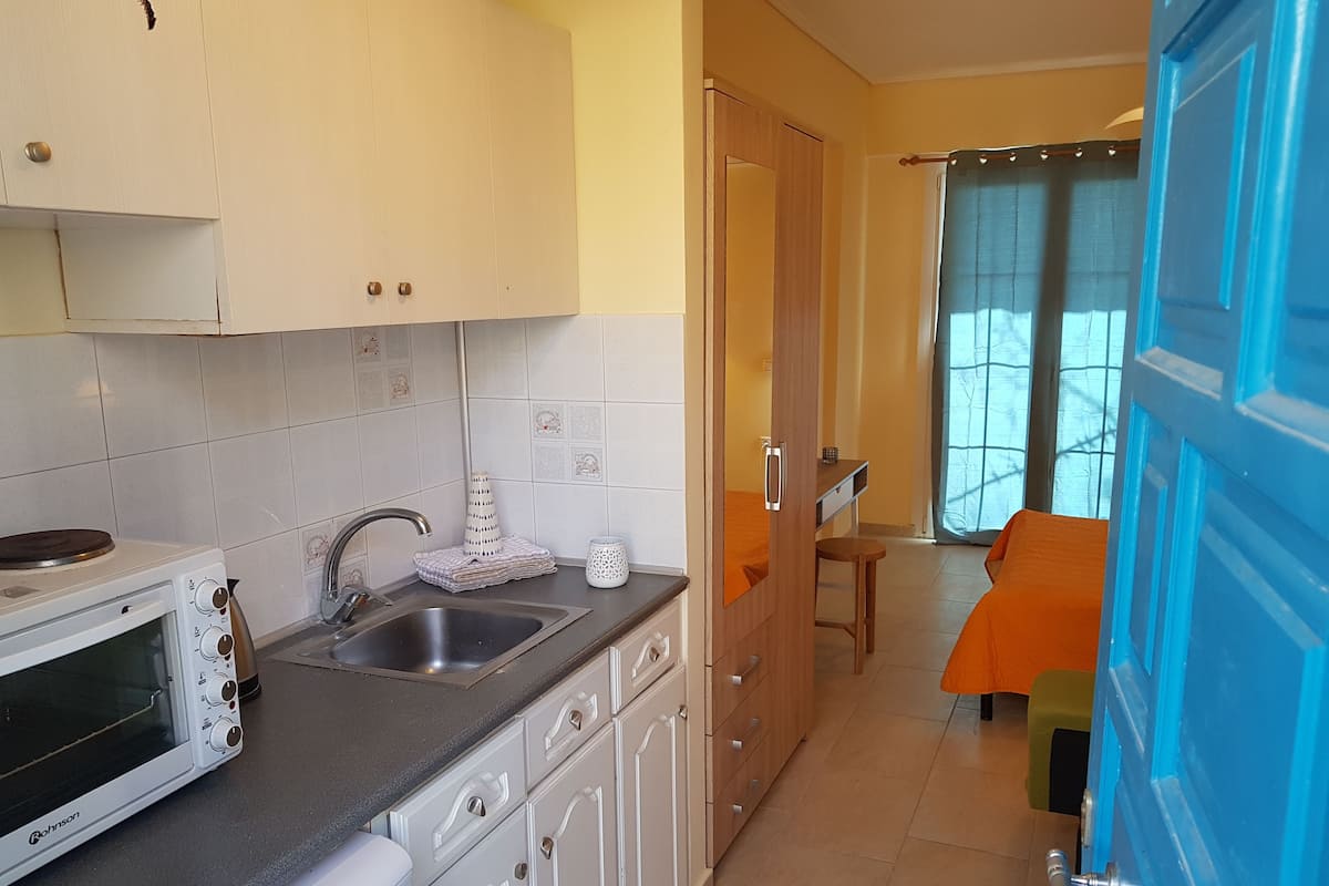 Cocina compacta con microondas, pileta y alacenas. En el fondo, se observa un comedor con mesa y sillas.